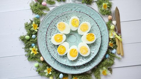 Easter table setting with flowers and eggs. Decorative ceramic plates with boiled eggs halfs. Rustical dishware. View from above.