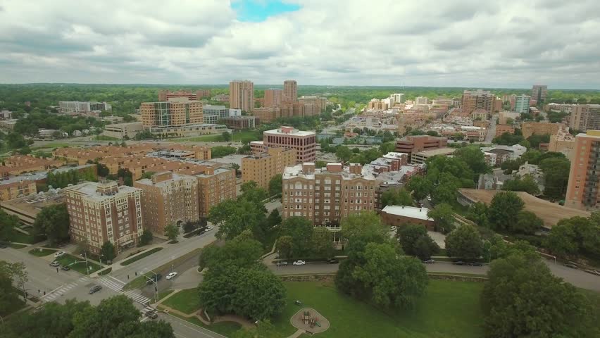 Aerial view moving down over the Kansas City skyline and behind trees, during the day.