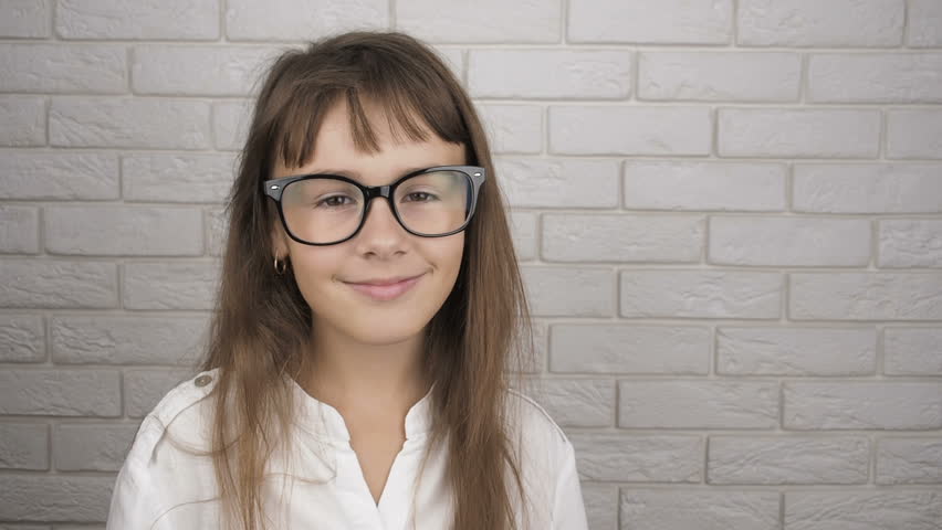 A child with glasses shows ok. The little girl looks through the gesture ok.