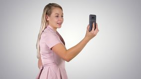 Female in pink dress making video call with her smart phone on gradient background.