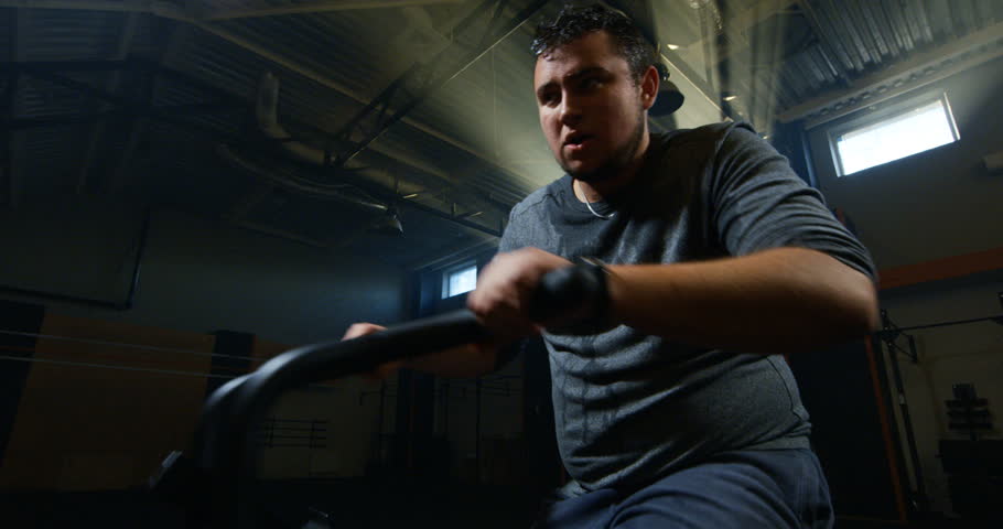 Medium shot of an overweight young man taking a break then continue intense workout on an exercise bike shot on Red camera 4K