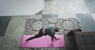 From the high top capturing video of a lady practicing yoga at home in living room on the mat , she make hard exercises and poses.