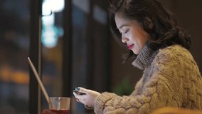 Side view of one pretty young Asian woman playing with mobile phone in hand by the cafe window, Beautiful Chinese girl with mobile technology lifestyle in the city 4k clip