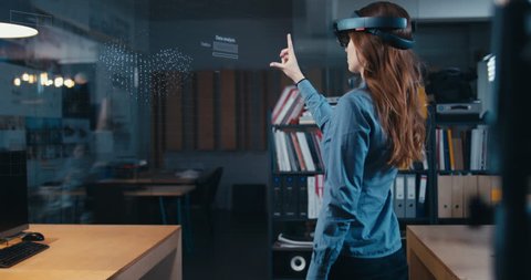 Young adult female using holographic augmented reality glasses in trendy office. Future concept. Generic big data interface added 