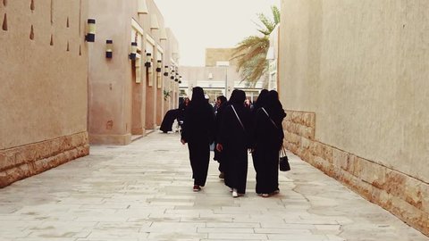 Riyadh / Saudi Arabia - February 22, 2019: Arabian ladies in traditional clothing called abaya walk along a street of mudhouses in Saudi's Albujairi square at Historical Diriyah 