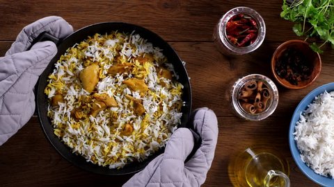 Biryani with chicken. Traditional Indian dish of rice and chicken marinated in spices and yoghurt.Top view. Putting ready dishes on the table. Slow motion.