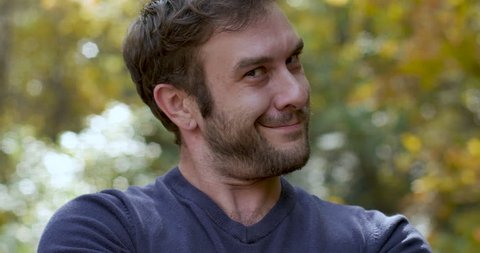Attractive young man with a beard in his 30s pops into frame smiling and looking smugly at the camera