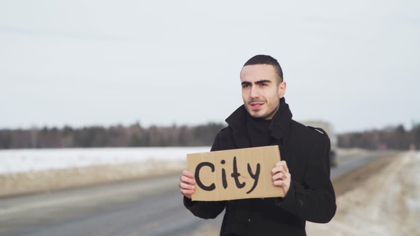 Man hitchhiking at winter country road with cardboard plate and asking someone to stop closeup 4k