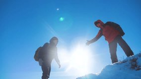 teamwork tourists winter snow business travel trip lends a helping hand. two men with backpacks hiking help each other silhouette in mountains with sunlight. slow motion video. rock climbers teamwork