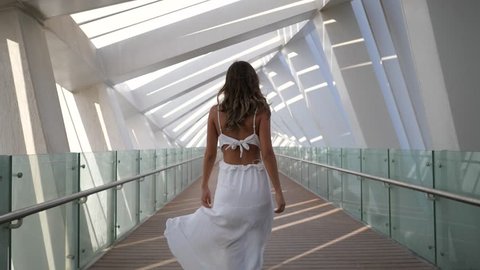 SLOW MOTION: Beautiful sensual woman fashion portrait with long white dress walking on modern bridge in Dubai.