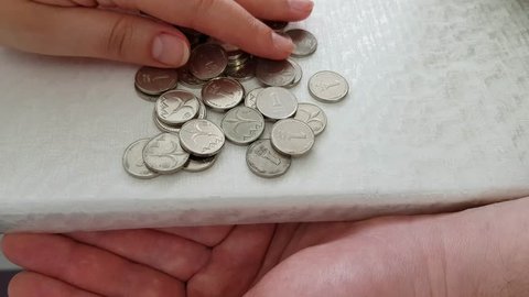 one person moves slowly Israeli one shekel coins on white table so they fall from the edge to another person hand palm