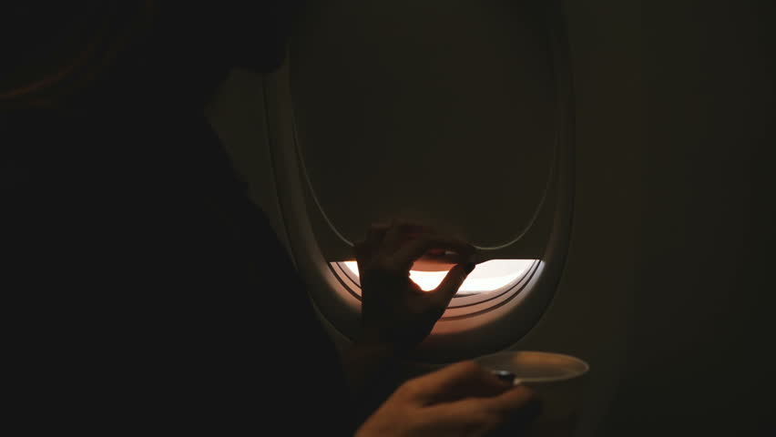 Close-up shot of happy female passenger opening airplane window, enjoying hot drink and amazing sunny view during flight | Shutterstock HD Video #1024987604