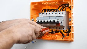 Video of the hands of the electrician technician who inserts and blocks the cable in a circuit breaker in the electrical panel of a residential installation. Construction industry.