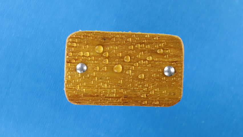 Top view, rotation of light wooden plank with iron bolts in raindrops. Isolated