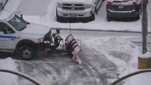 Coquitlam, BC, Canada - March 23, 2018 : Slow motion of compact tractor with snow plowing equipment cleaning parking lot on cold blizzard snow winter day