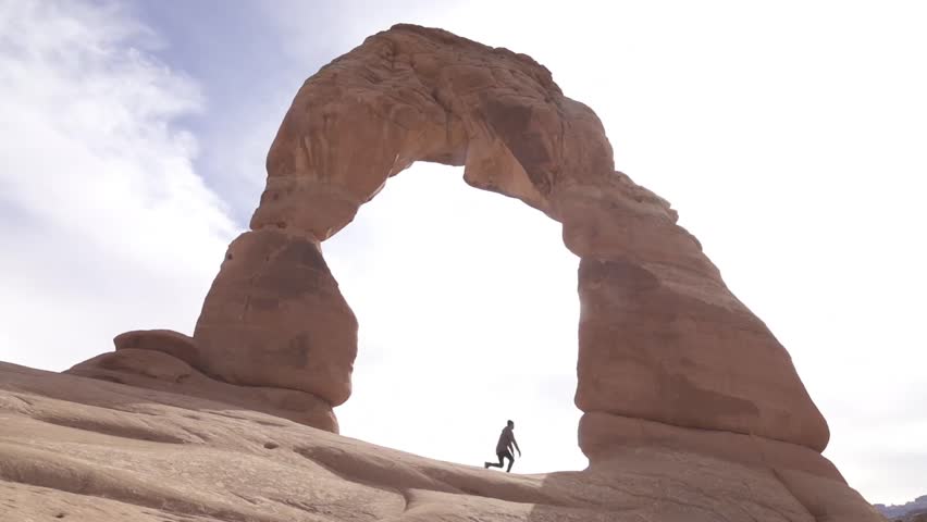 Amazing slow motion shot of man doing a movement, a wall flip under monolithic natural stone arch in Arches National Park
