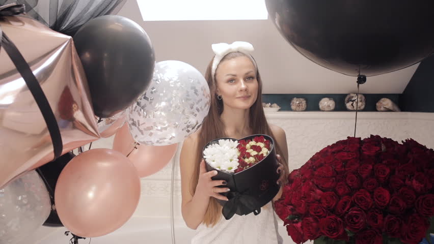 Happy birthday girl clapping hands in bathroom with bouquet and air balloon.