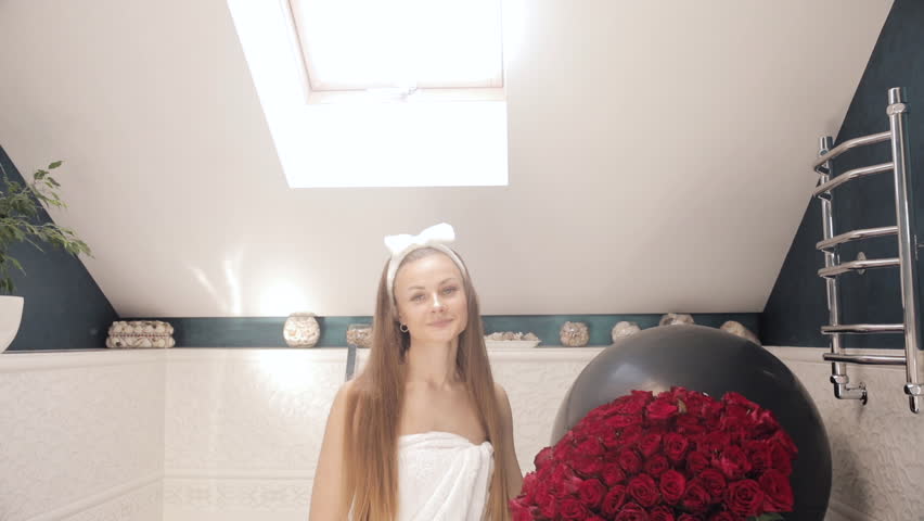 Happy birthday girl clapping hands in bathroom with bouquet and air balloon.