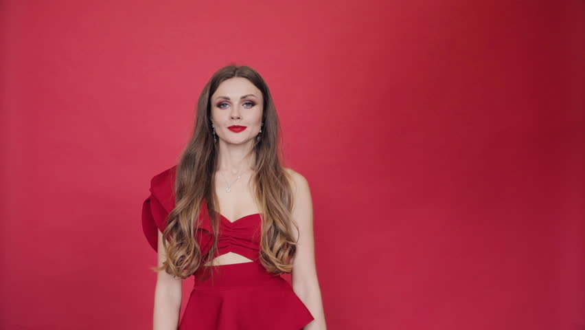 Footage of beautiful young brunette woman wearing gorgeous stylish red dress and make up with big black air balloon with text helloo thirties 30. Isolate on red background.
