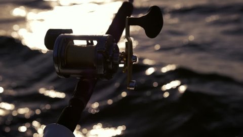 Trolling fishing on the sea by boat. Silhouette of a fishing reel in the backlight. Fishing atmosphere. Sunset while fishing.