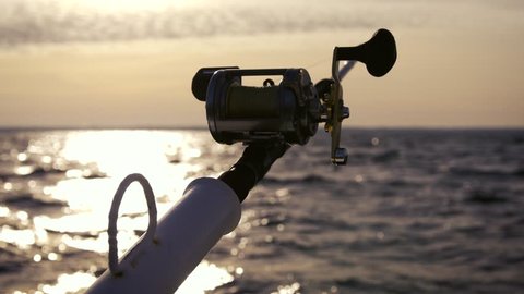 Trolling fishing on the sea by boat. Silhouette of a fishing reel in the backlight. Fishing atmosphere. Sunset while fishing.