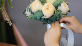 A young girl works in a flower shop, ties a ribbon bow to the finished composition. "Bouquet design - delicate beige roses with eucalyptus and brunia albiflora". - Powered by Shutterstock - Get 15% off with code: PIKWIZARD15