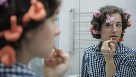 Woman paints her lips looking in the mirror in her bathroom
