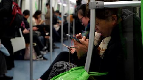 SHANGHAI - MARCH 21, 2018: Unidentified Aged lady sit at metro car, look to smartphone and yawn, slow motion shot. Chinese woman stare to mobile device and slowly open mouth, tired at evening time