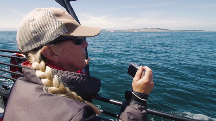Woman on whale watching boat with camera waits to see animals