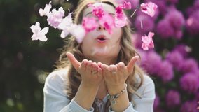 Woman Enjoying Spring Blossom. SLOW MOTION. Happy Smiling Girl blowing on rhododendron flower petals, making them fly to camera. Sunny Spring Outdoors Activity, Lens Flare. - Powered by Shutterstock - Get 15% off with code: PIKWIZARD15