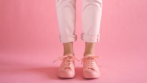 Close up of shapely young female legs walking in fashionable sneakers on coral background