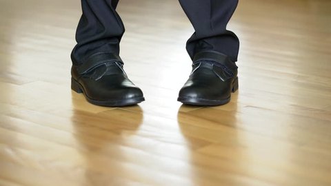 Legs of a man in black shoes dancing elements of dubstep on the brown floor background. View shot looking straight at the shoes and legs in black trousers.
