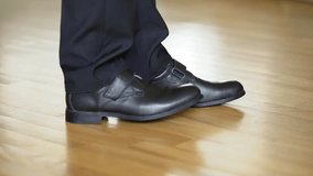 Man in black leather shoes dancing on the wooden floor. Male's legs in black trousers and new shoes shows some kind of dance on a parquet. Close-up