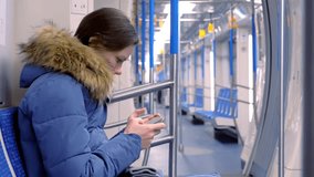 Woman rides in an empty subway car and watches a video on her smartphone. Side view.