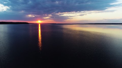 Aerial view. Amazing sky reflected in water. Beautiful sunset over the lake. landscape, in background horizon and forest. Orange or yellow sun penetrates through fluffy or airy gray or white clouds