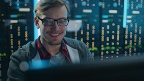 Portrait of a Smart Focused Young Man Wearing Glasses Working on a Desktop Computer. In the Background Technical Department Office with Functional Data Server Racks. - Powered by Shutterstock - Get 15% off with code: PIKWIZARD15