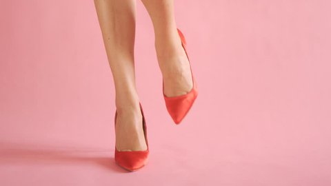 Close up of shapely female legs dancing in sexy red high hells on coral background
