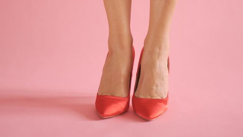 Close up of shapely female legs dancing in sexy red high hells on coral background