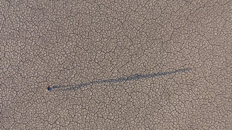 Climate change.zoom out high aerial view of a devastated farmer walking across the cracked mud surface of a dry dam due to drought from climate change and global warming