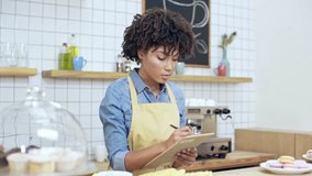 beautiful african american female cashier writing in clipboard behind counter in cafe