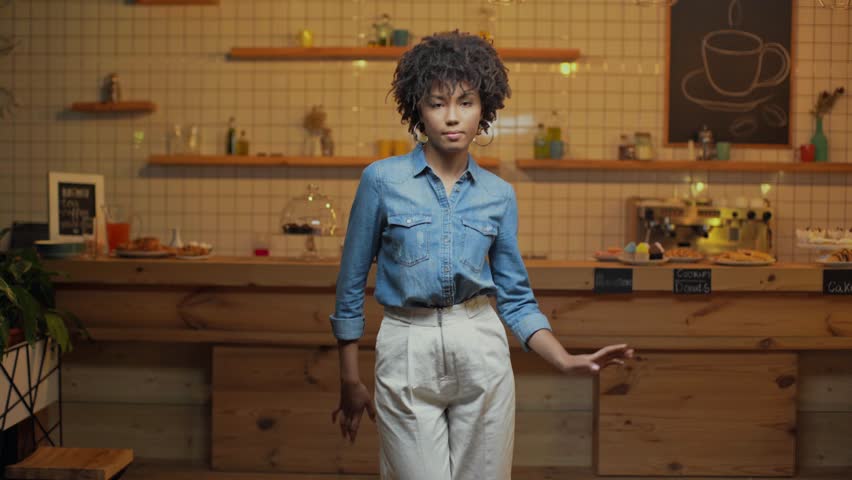 beautiful african american female cafe owner in denim blouse dancing, smiling and looking at camera in cafe Royalty-Free Stock Footage #1025060375