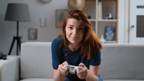 Determined girl playing a video game at home. Excited gamer woman sitting on a couch, playing and losing in video games on a console, using a wireless controller. Cozy room, lovely home atmosphere.
