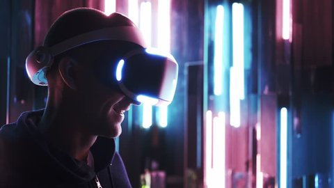 Portrait men in modern VR headset turning head around, looking virtual reality in google's in dark space at background colored neon lamps