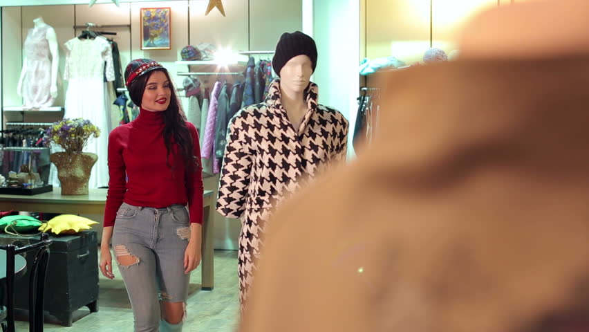 A young girl in jeans and a red sweater buys clothes in a clothing store, she looks at the coat that hangs on a mannequin.