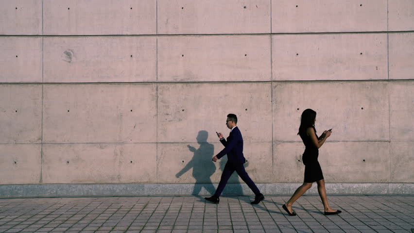 Young male and female business people in formal wear walking on street looking at their smartphones ignoring each other addicted to social networks.Antisocial millennials, technology and communication Royalty-Free Stock Footage #1025068373