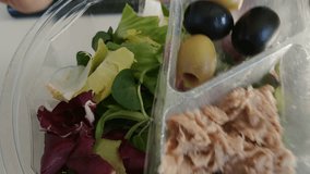 Preparation of a takeaway salad, removed the lid we find a container with olives and tuna to be poured on the leaves of red and green lettuce. Pour the contents and throw the container. Video 25fps 4K