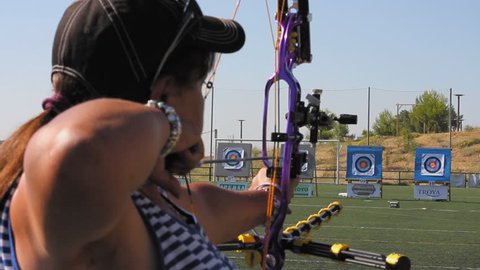 Madrid, Spain. July 2016. Side view of  female compound bow archer and targets in the background.