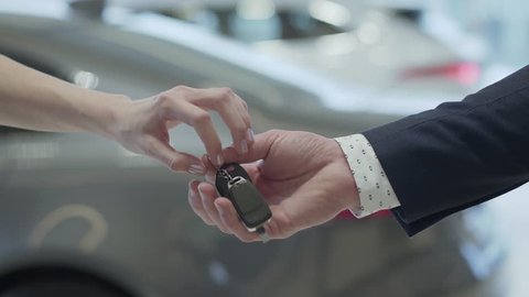 Male hand gives a car keys to famale hand in the car dealership close up. Unrecognized auto seller and a woman who bought a vehicle shake hands.