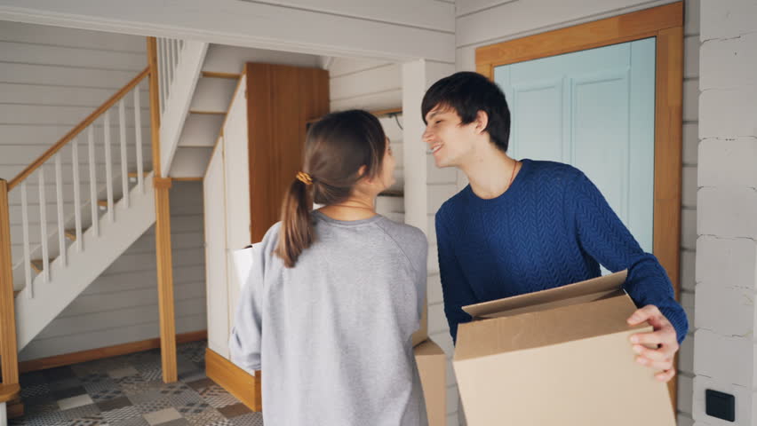 Man and woman with carton boxes are opening door, entering their new house, looking around and kissing then going upstairs carrying things. Relocation and family concept. | Shutterstock HD Video #1025077898