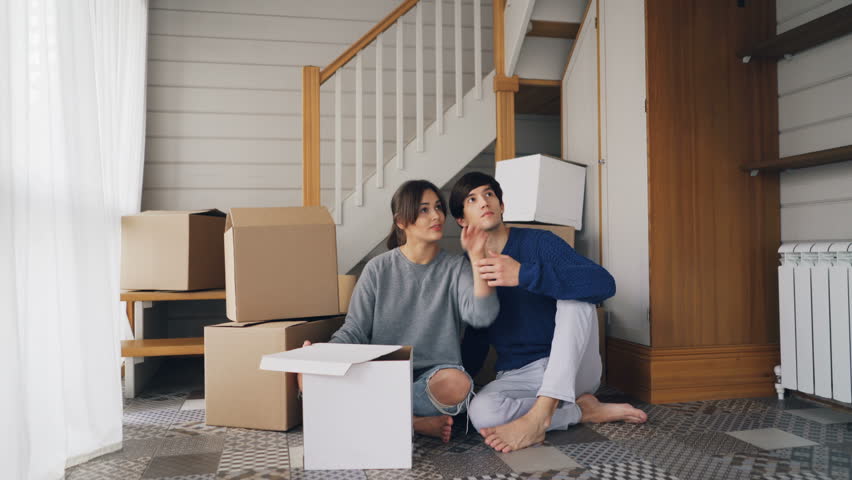 Girlfriend and boyfriend are talking making plans sitting on floor of new purchased house, looking around and expressing positive emotions. Relationship and relocation concept. | Shutterstock HD Video #1025077907